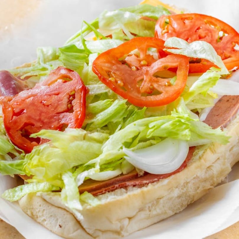 A close-up of a Bellagio Wings & Pizza sub sandwich, filled with lettuce, tomatoes, onions, and deli meats.