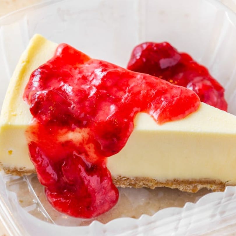 A slice of cheesecake with a graham cracker crust, topped with bright red strawberry sauce.
