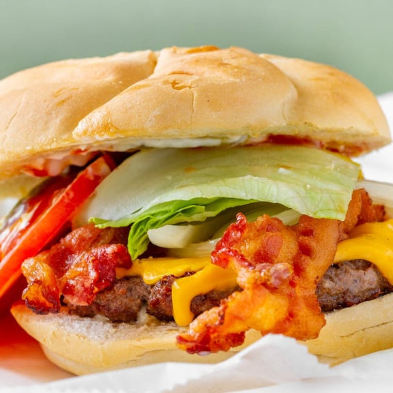 Close-up of a bacon cheeseburger with lettuce, tomato, and onions on a bun.