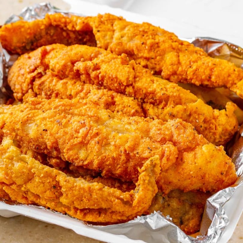 Crispy, golden-brown fried fish fillets, seasoned with spices, served in a foil-lined container.