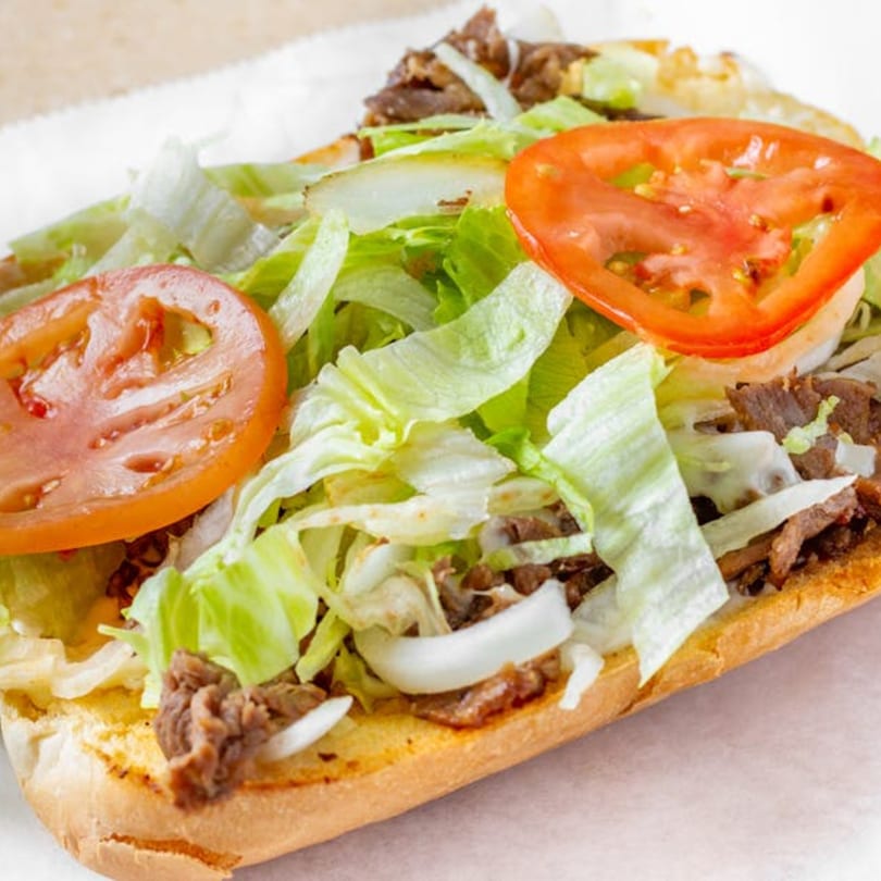 A close-up of a Bellagio steak and cheese sub with lettuce, tomatoes, and onions.